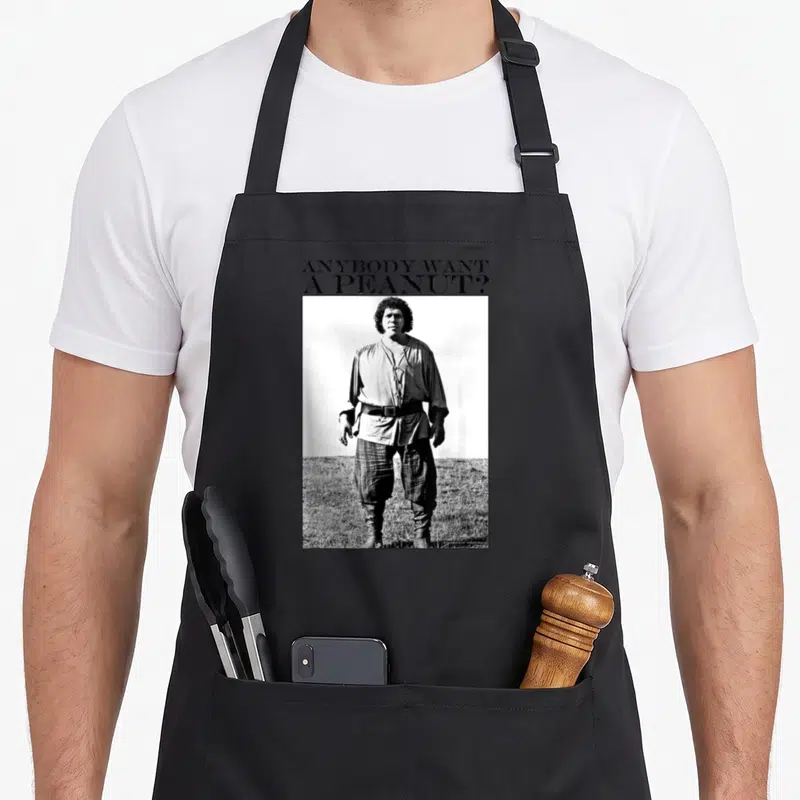 Anybody princess apron - ANYBODY WANT A PEANUT? text above a black and white photo of a man standing in a field — shown on a black cotton canvas apron against a white background