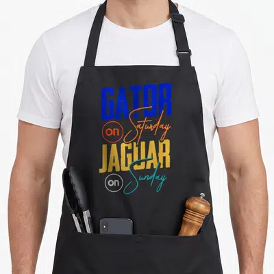 Saturday florida apron - Stacked GATOR on Saturday JAGUAR on Sunday text in blue orange yellow and teal — shown on a black cotton canvas apron against a white background
