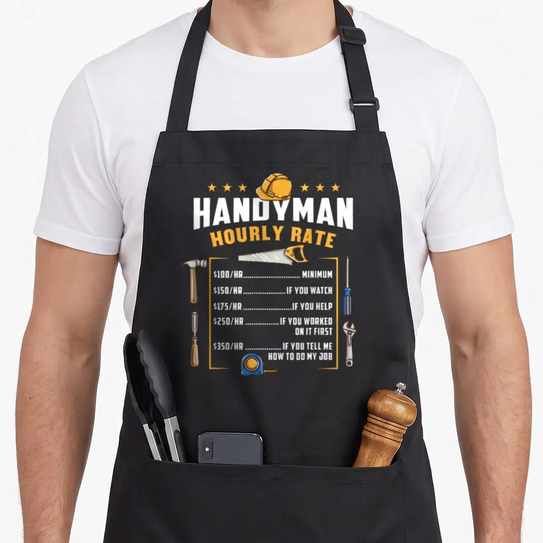 Rate handyman apron - Cartoon hard hat and tools framing a sarcastic hourly rate price list in orange and blue — shown on a black cotton canvas apron against a white background