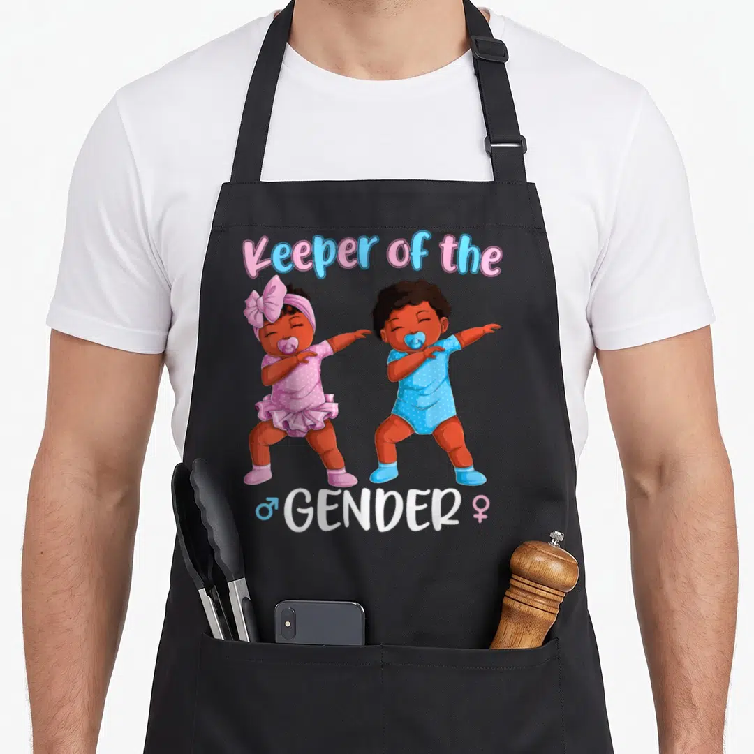 Baby gender reveal co apron - Two cartoon babies dabbing under Keeper of the Gender text with pink and blue accents — shown on a black cotton canvas apron against a white background