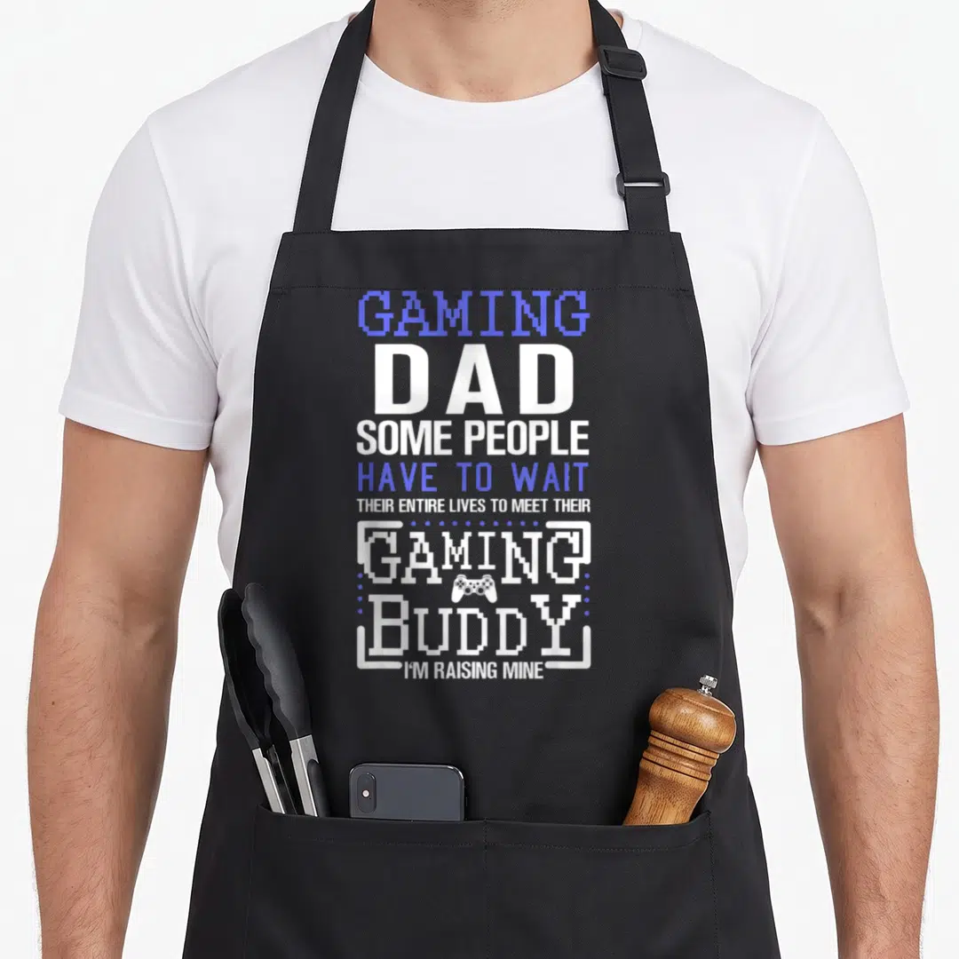 Father gaming apron - Stacked white and blue text reading Gaming Dad with a small game controller icon centered below — shown on a black cotton canvas apron against a white background
