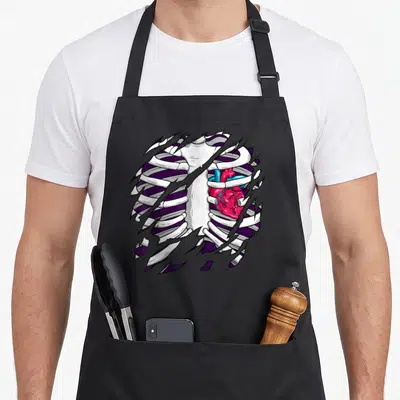 Cage x ray apron - Realistic red heart inside white rib cage with torn fabric edges on purple background — shown on a black cotton canvas apron against a white background