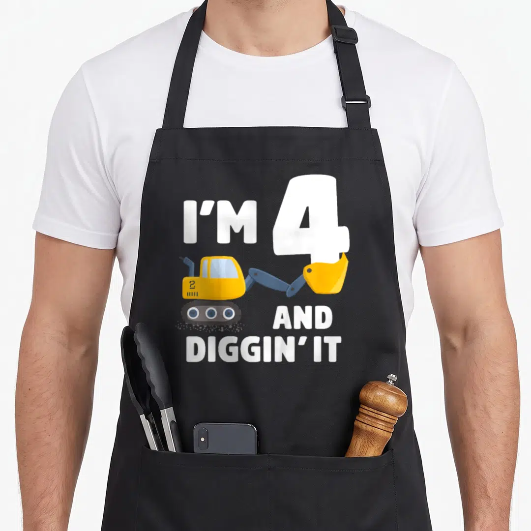 Birthday four truck apron - I'M 4 AND DIGGIN' IT text with yellow excavator and blue details — shown on a black cotton canvas apron against a white background