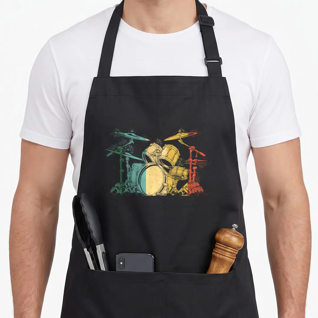Drummer drums apron - Drum kit graphic split vertically into green, yellow, and red distressed color zones — shown on a black cotton canvas apron against a white background
