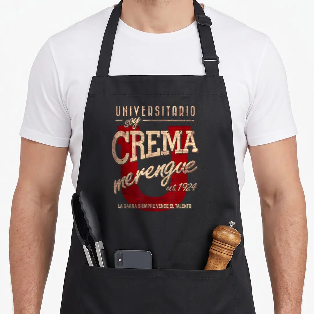 Universitario merengue apron - Red letter U with beige distressed text UNIVERSITARIO soy CREMA merengue and La Garra — shown on a black cotton canvas apron against a white background