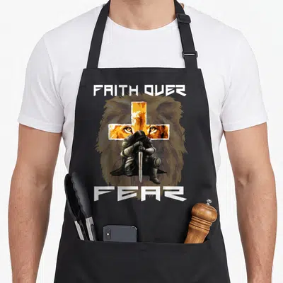 Fear prayer apron - Kneeling knight holding sword before orange cross and grey lion head with white text — shown on a black cotton canvas apron against a white background