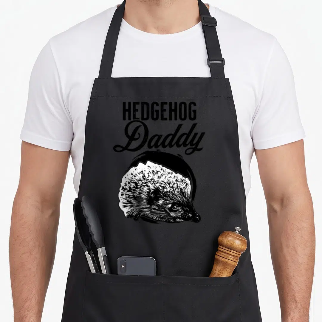 Hedgehog father daddy apron - Realistic hedgehog head below stacked HEDGEHOG Daddy text in black and white — shown on a black cotton canvas apron against a white background