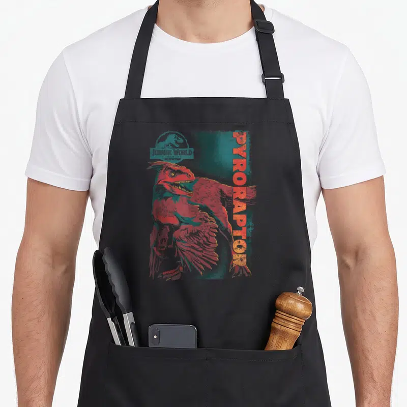 Dominion jurassic world apron - Distressed red-orange and teal Pyroraptor illustration with Jurassic World Dominion logo — shown on a black cotton canvas apron against a white background