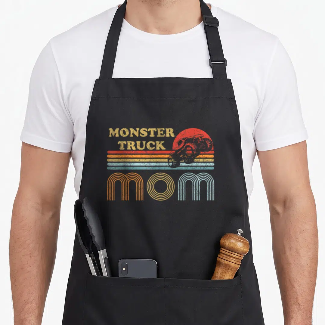 Horizon truck apron - Retro MONSTER TRUCK MOM graphic with red sun and five colored horizontal stripes — shown on a black cotton canvas apron against a white background