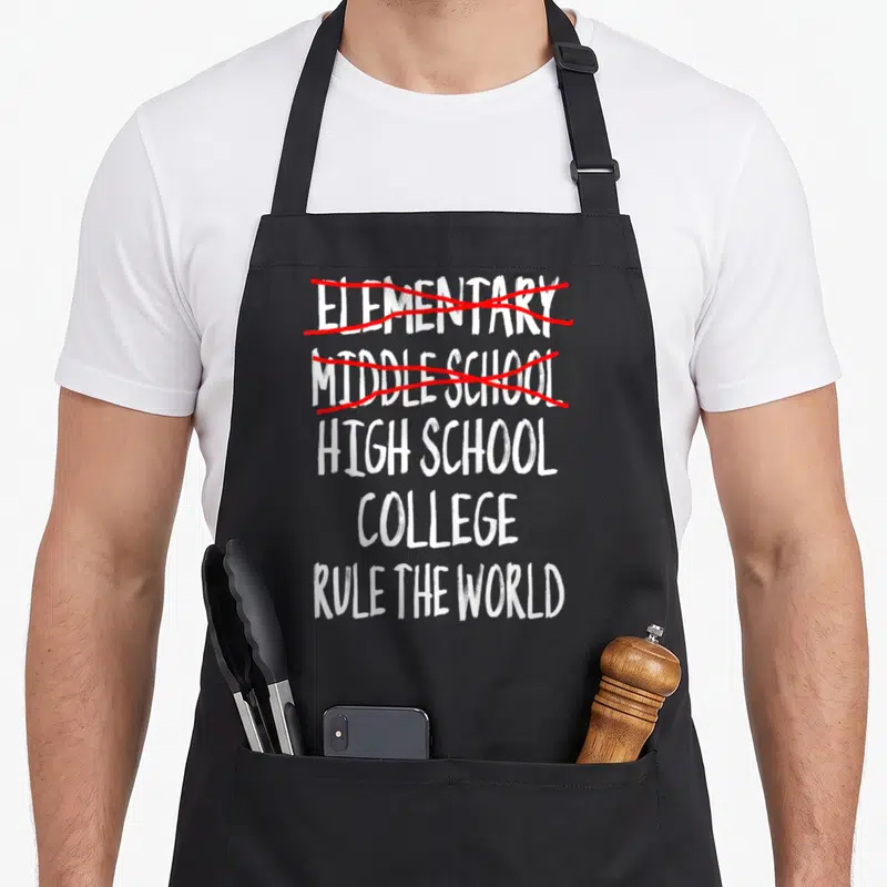 School junior apron - Stacked white text crossing out elementary and middle school with red scribbles above high school — shown on a black cotton canvas apron against a white background