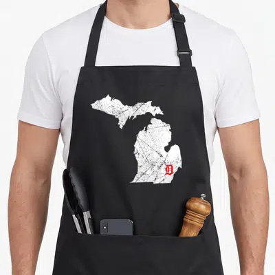 Map detroit apron - Distressed white Michigan map with red Old English D in southeast region — shown on a black cotton canvas apron against a white background