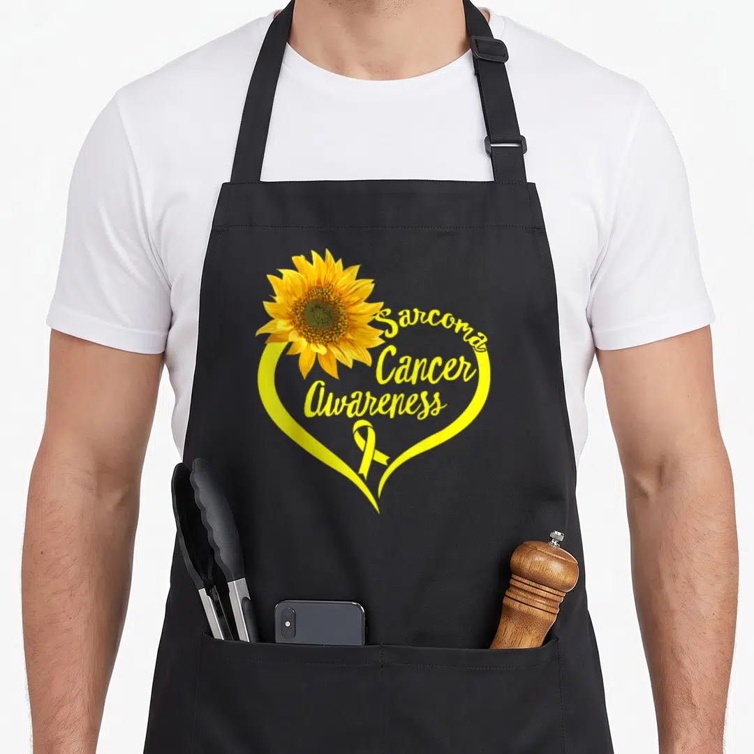 Ribbon sunflower apron - Yellow heart with sunflower and Sarcoma Cancer Awareness text — shown on a black cotton canvas apron against a white background