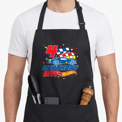 4th wheel apron - Red number 4 blue race car BIRTHDAY BOY text checkered flag confetti — shown on a black cotton canvas apron against a white background