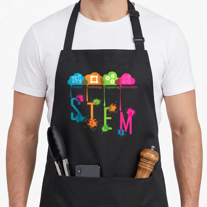 Stem science apron - Four colored clouds with icons dripping paint onto large STEM letters — shown on a black cotton canvas apron against a white background