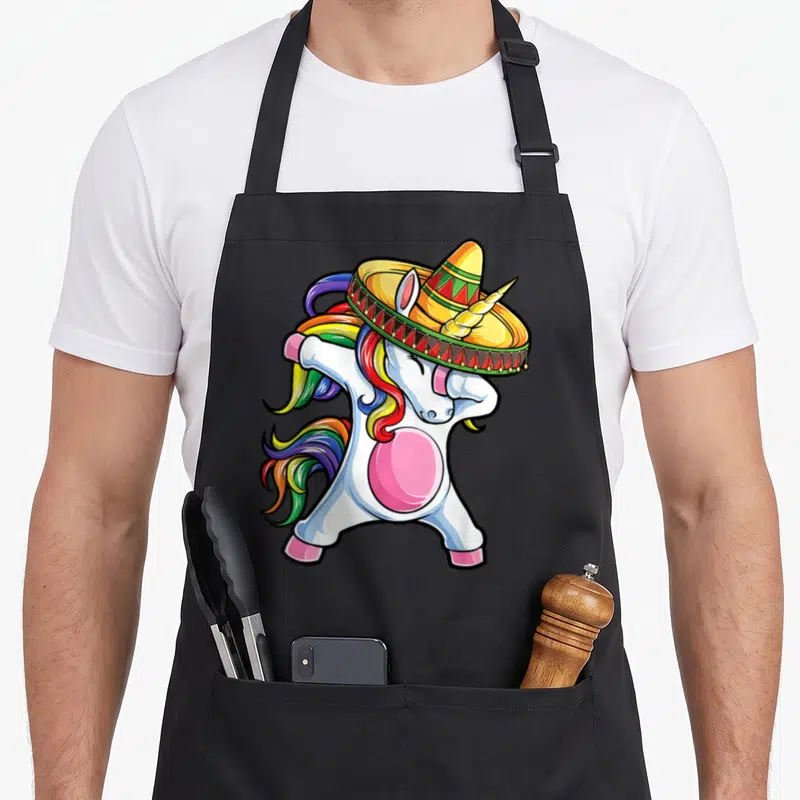 Unicorn mexican apron - Cartoon white unicorn dabbing while wearing a colorful sombrero with rainbow mane — shown on a black cotton canvas apron against a white background