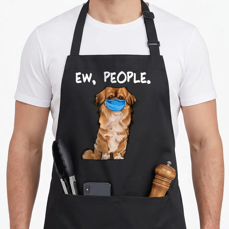Pekingese dog face apron - Cartoon brown dog wearing a blue mask under white ew people text — shown on a black cotton canvas apron against a white background