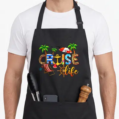 Cruise summer vacation family aprons - Cartoon graphic with CRUISE letters filled with patterns, palm trees, anchor — shown on a black cotton canvas apron against a white background