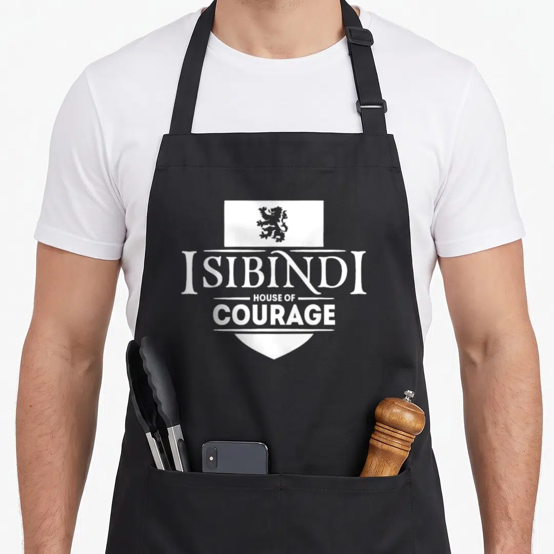 Isibindi school apron - White shield with lion and stacked text ISIBINDI HOUSE OF COURAGE on black apron — shown on a black cotton canvas apron against a white background