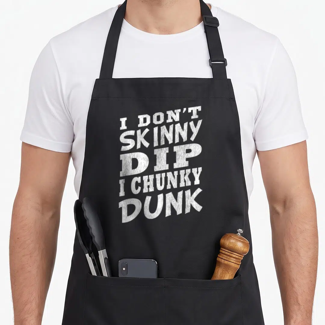 Skinny dip apron - White distressed text reading I DON'T SKINNY DIP I CHUNKY DUNK stacked on black fabric — shown on a black cotton canvas apron against a white background