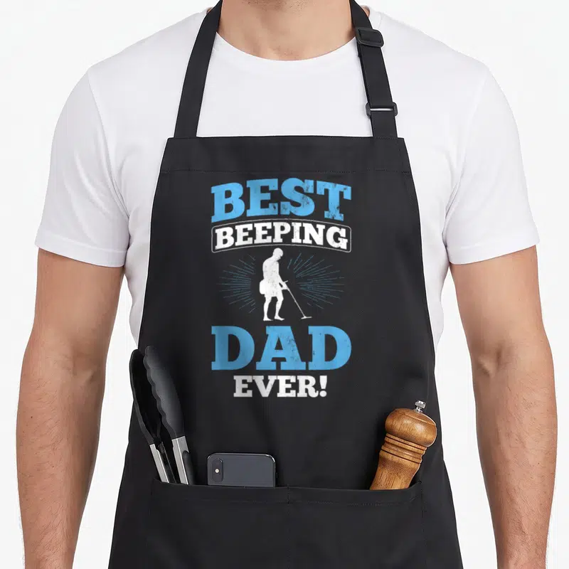 Beeping metal detecting apron - Distressed blue and white text stacking around a white metal detectorist silhouette — shown on a black cotton canvas apron against a white background