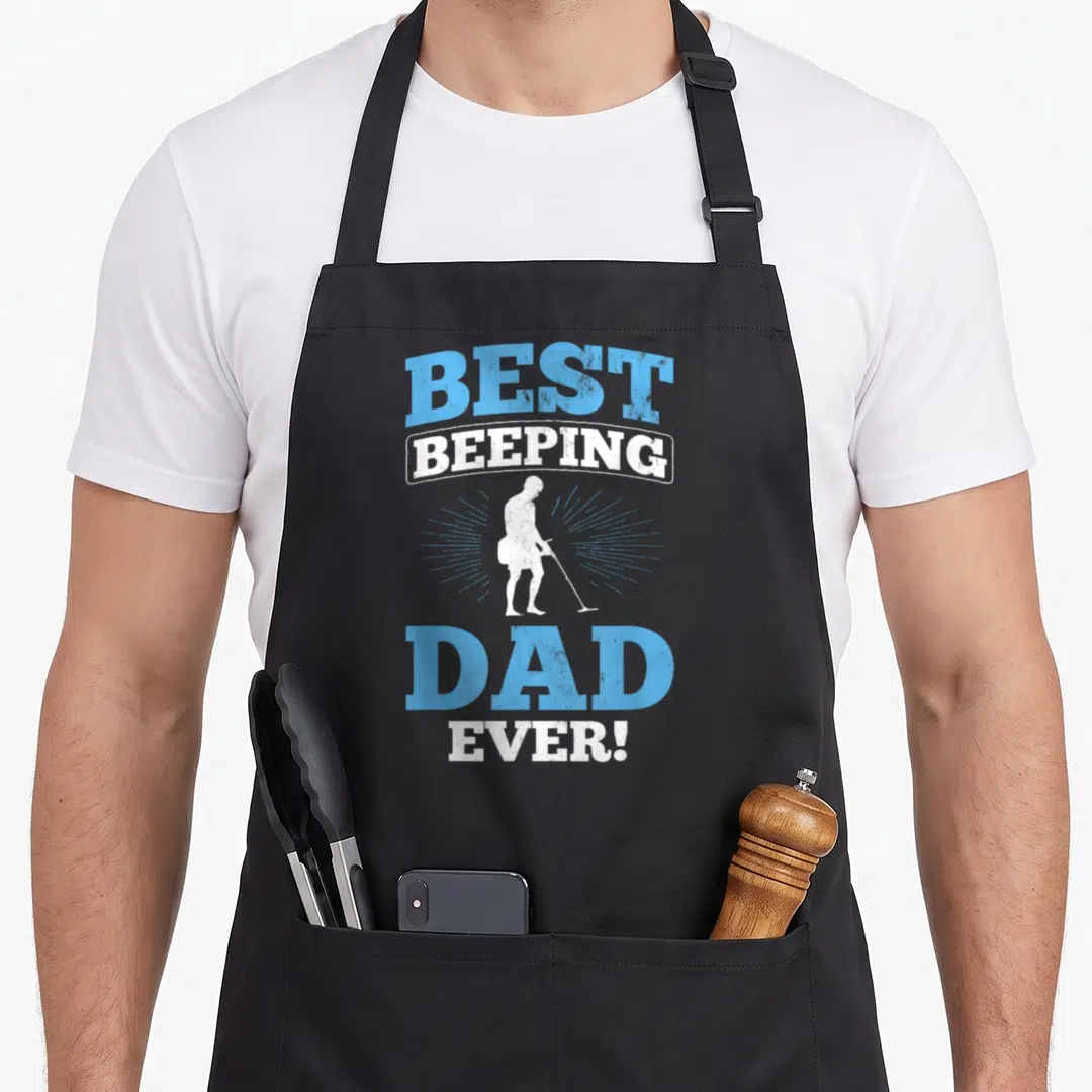 Beeping metal detecting apron - Distressed blue and white text stacking around a white metal detectorist silhouette — shown on a black cotton canvas apron against a white background