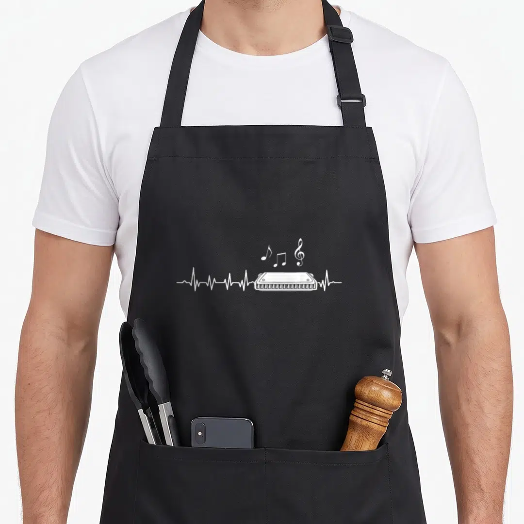 Musician harmonica apron - White harmonica on heartbeat line with musical notes and treble clef — shown on a black cotton canvas apron against a white background