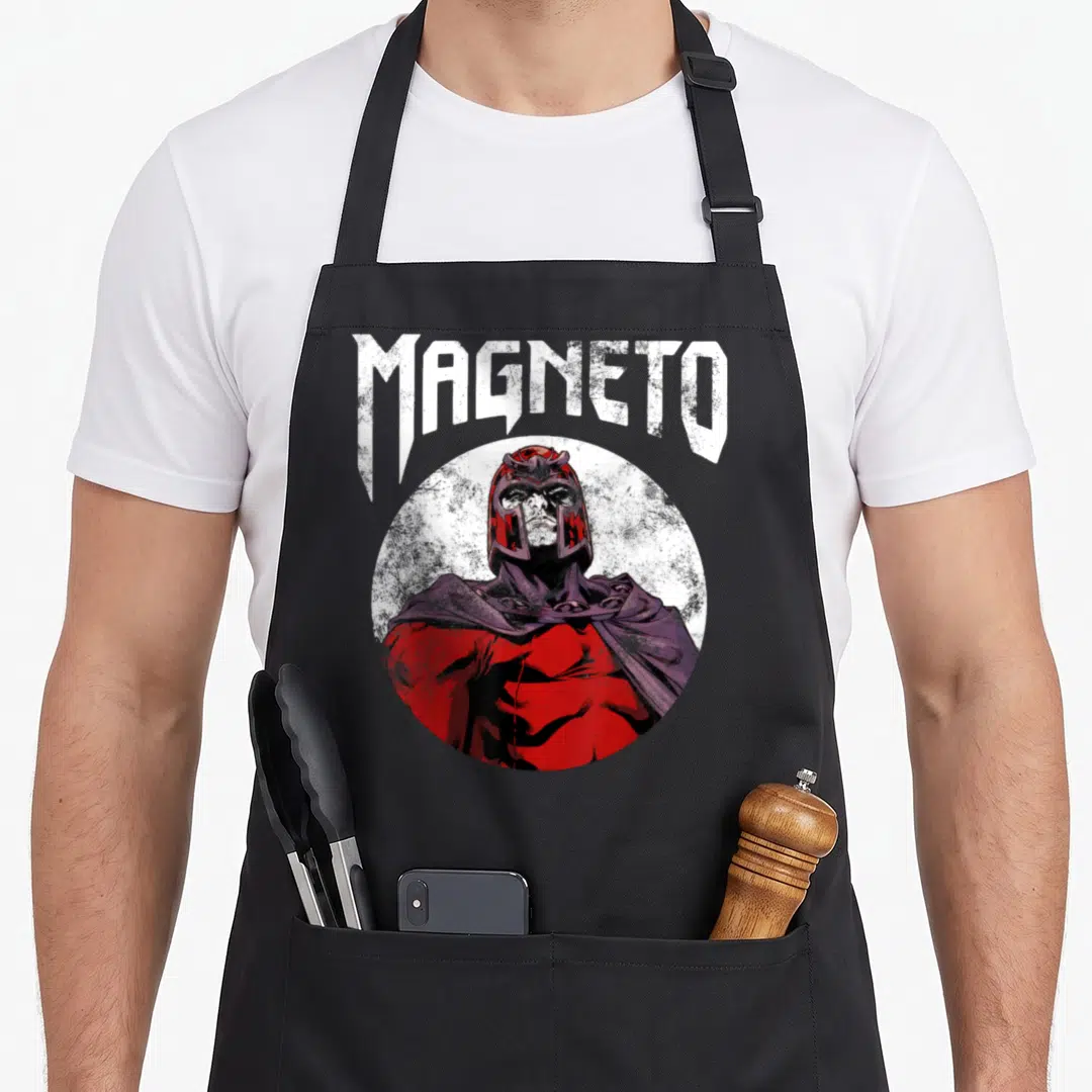 Magneto x apron - MAGNETO text arched over circular comic portrait in red white purple — shown on a black cotton canvas apron against a white background