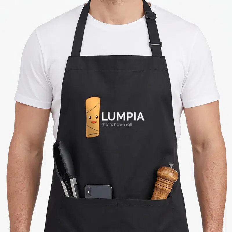 Lumpia spring apron - Cartoon orange lumpia character next to white text reading LUMPIA that's how i roll — shown on a black cotton canvas apron against a white background