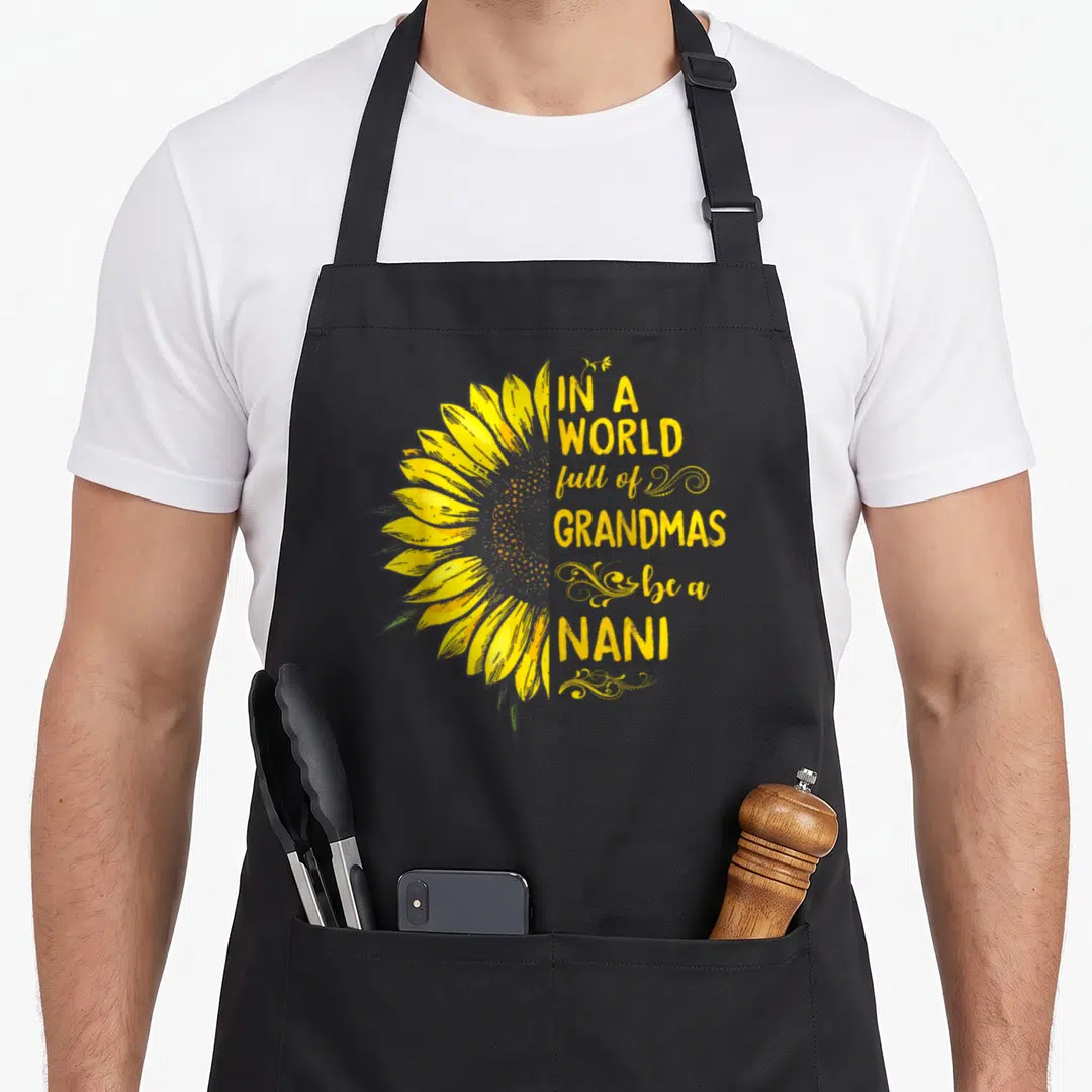 Nani grandma's aprons - Yellow watercolor sunflower next to stacked text reading IN A WORLD full of GRANDMAS be a NANI — shown on a black cotton canvas apron against a white background