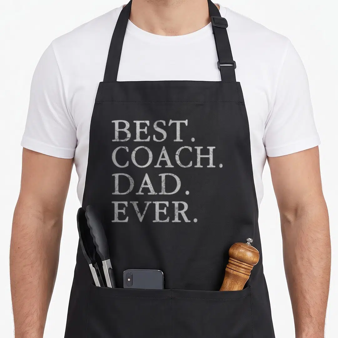Hockey football apron - White distressed text reading BEST. COACH. DAD. EVER. stacked on four lines — shown on a black cotton canvas apron against a white background