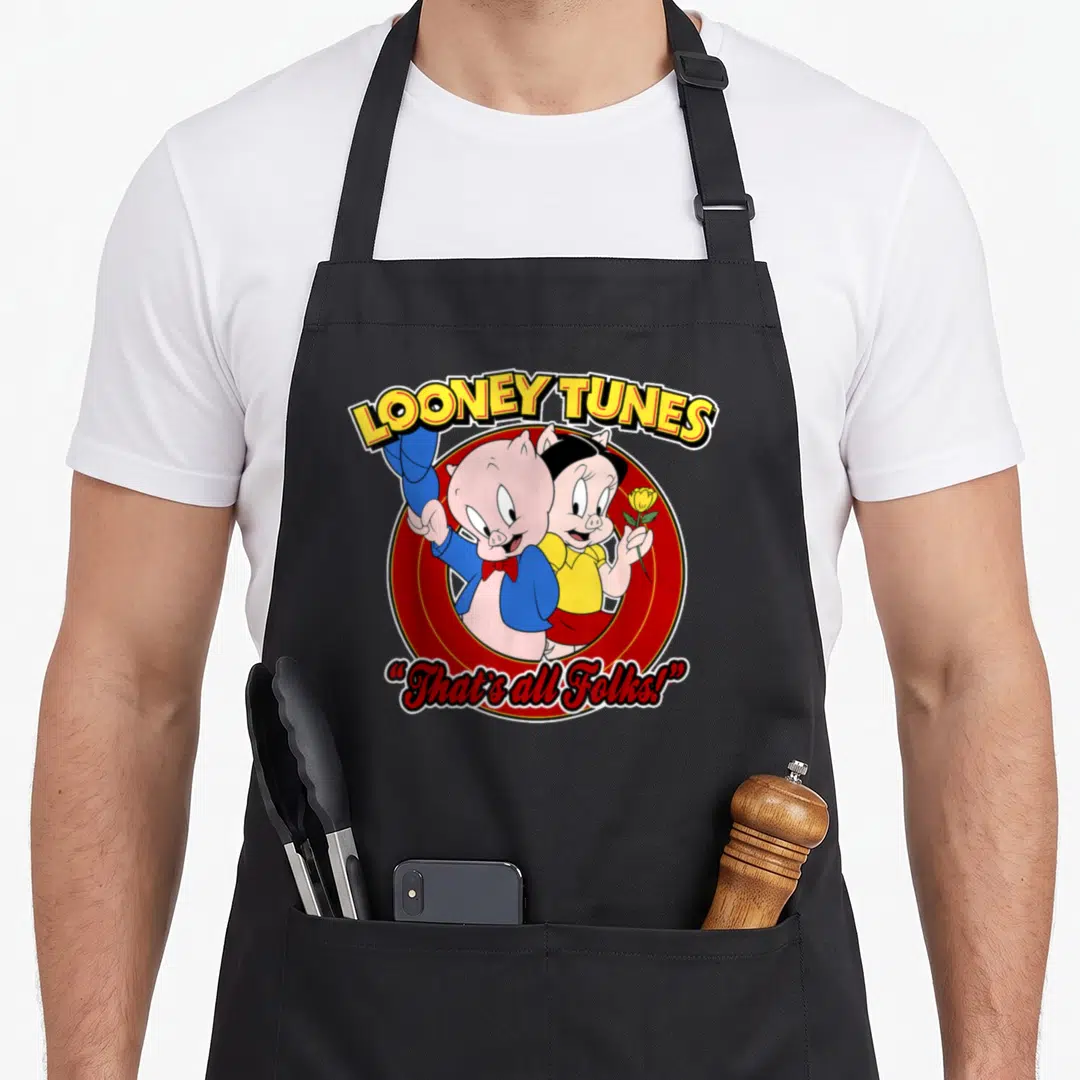 Porky petunia apron - Two cartoon pigs in red circle with LOONEY TUNES and That's all Folks text — shown on a black cotton canvas apron against a white background