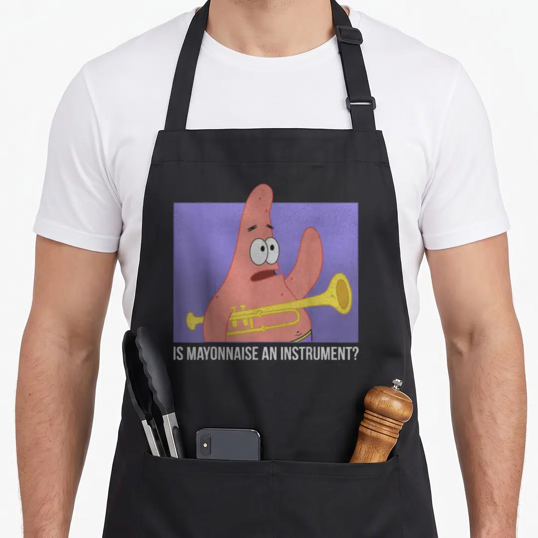 Mayonnaise patrick apron - Patrick Star holding yellow trumpet on purple background with white text IS MAYONNAISE — shown on a black cotton canvas apron against a white background