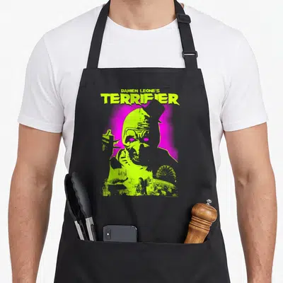 Glowing clown aprons - Terrifier Art the Clown lime green magenta ferris wheel cartoon print — shown on a black cotton canvas apron against a white background