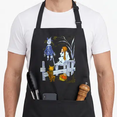 Toto dorothy apron - Line art of scarecrow, girl on fence, dog, and basket in blue orange white yellow — shown on a black cotton canvas apron against a white background