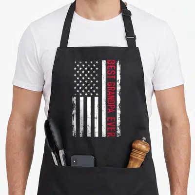 Grandpa american flag apron - Vertical BEST GRANDPA EVER text on distressed white and red USA flag stripes — shown on a black cotton canvas apron against a white background