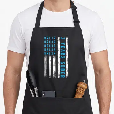 Addiction recovery day apron - Distressed vertical flag with blue ribbon grid and vertical 2 years sober text — shown on a black cotton canvas apron against a white background
