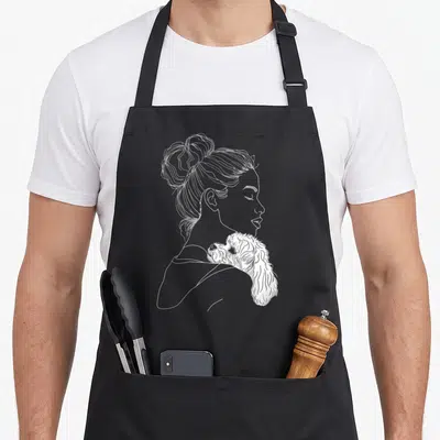 Frise mother's day aprons - White line art of woman profile with fluffy dog on shoulder — shown on a black cotton canvas apron against a white background