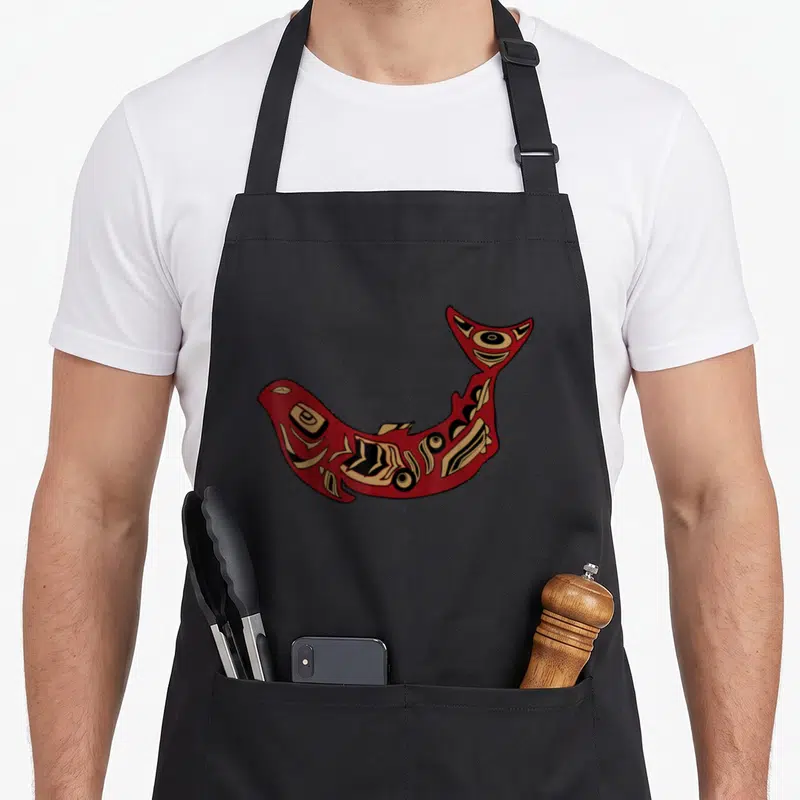 Salmon native american apron - Red and tan stylized fish with black indigenous patterns curved upwards on black fabric — shown on a black cotton canvas apron against a white background
