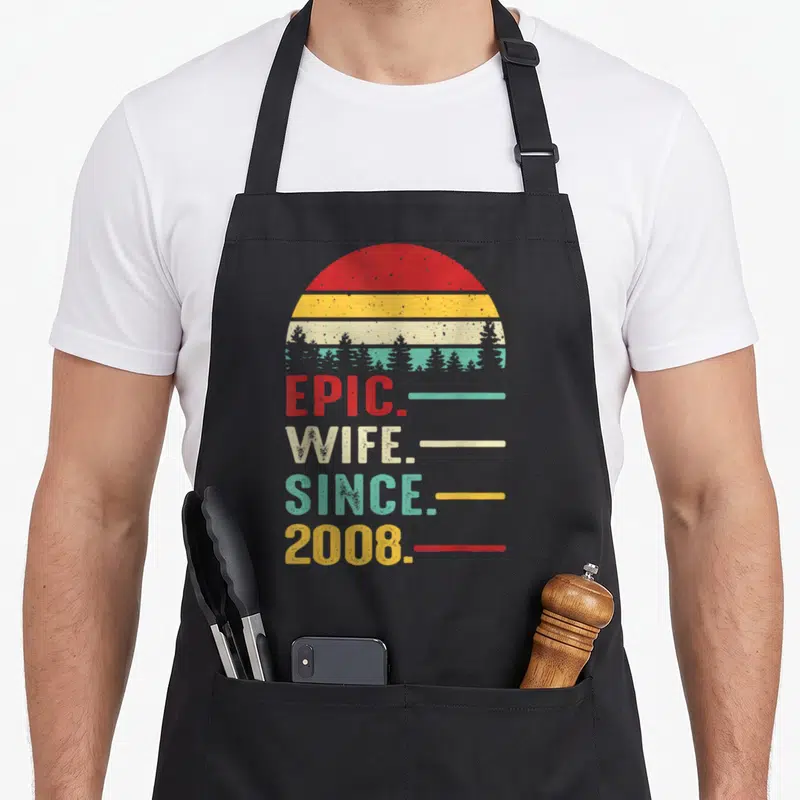 18th wedding apron - Retro sunset with tree silhouettes above stacked EPIC WIFE SINCE 2008 text lines — shown on a black cotton canvas apron against a white background