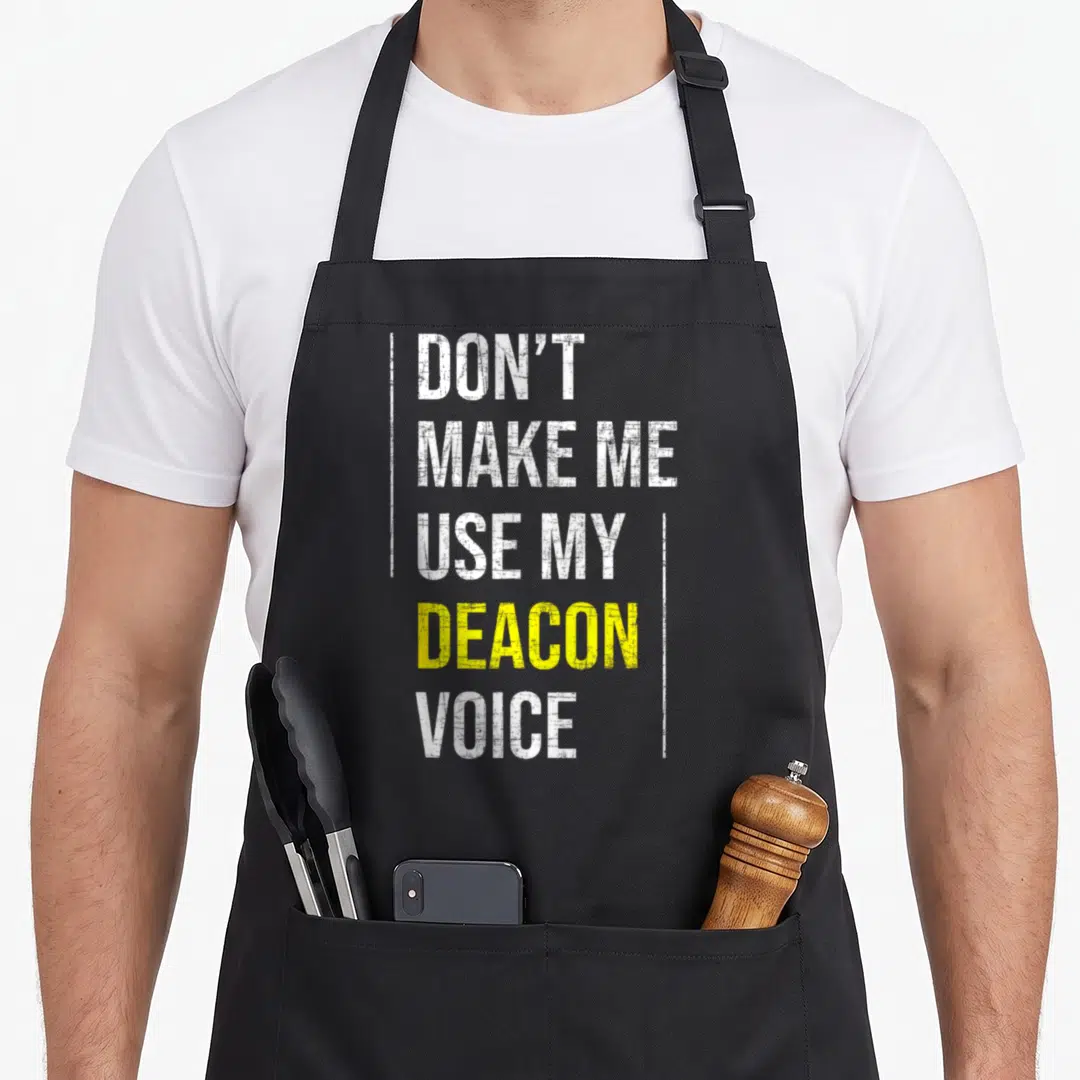 Use catholic apron - Stacked white and yellow text reading DON'T MAKE ME USE MY DEACON VOICE framed by vertical lines — shown on a black cotton canvas apron against a white background