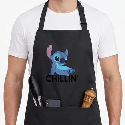 Chillin stitch apron - Blue cartoon character sitting above black CHILLIN' text — shown on a black cotton canvas apron against a white background