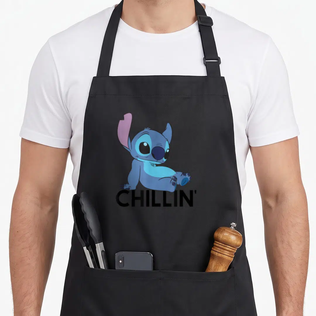 Chillin stitch apron - Blue cartoon character sitting above black CHILLIN' text — shown on a black cotton canvas apron against a white background