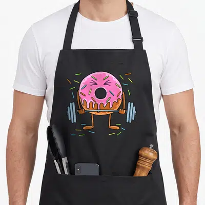 Weightlifing donut apron - Cartoon donut lifting barbell with pink frosting and colorful sprinkles — shown on a black cotton canvas apron against a white background