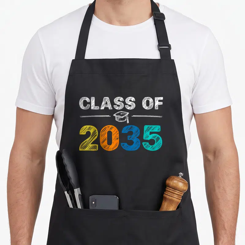 Graduation class grow apron - CLASS OF 2035 text with multicolored digits and white graduation cap sketch — shown on a black cotton canvas apron against a white background