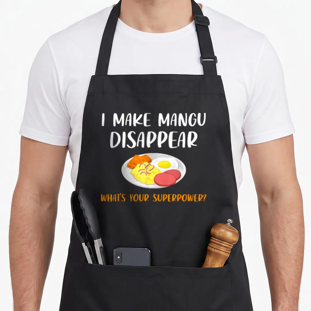 Superpower pride apron - Cartoon plate of mangu, sausage, egg, tostones with I Make Mangu Disappear text — shown on a black cotton canvas apron against a white background