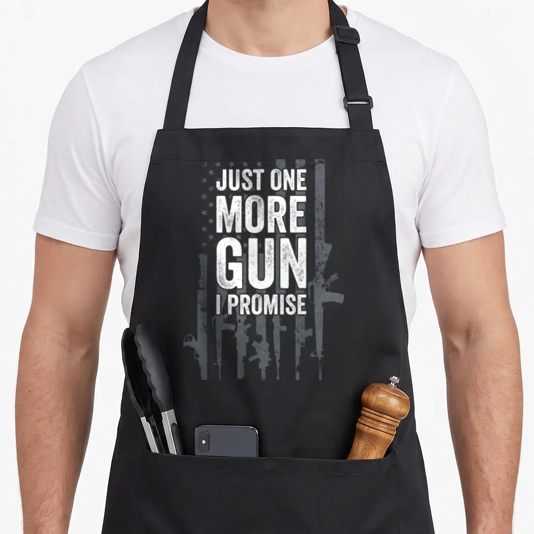 Soldier patriotic apron - Just one more gun I promise text over grey rifle silhouettes and stars — shown on a black cotton canvas apron against a white background