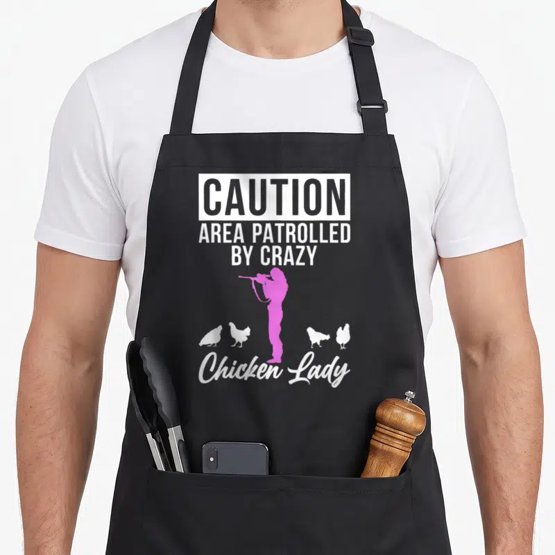Caution chicken apron - Pink woman silhouette with binoculars surrounded by four white chickens and caution text — shown on a black cotton canvas apron against a white background