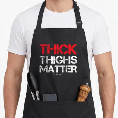 Matter thick aprons - Distressed red and white text reading Thick Thighs Matter stacked vertically — shown on a black cotton canvas apron against a white background