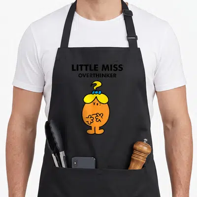 Miss meme apron - Orange cartoon character with yellow hair blue bow and question mark above black stacked text — shown on a black cotton canvas apron against a white background
