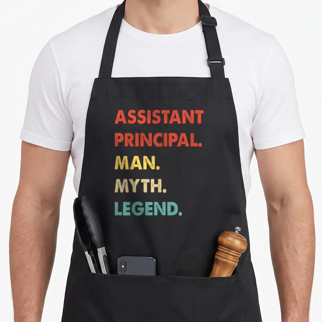 Assistant vice principal apron - Stacked red yellow beige and teal text reading Assistant Principal Man Myth Legend — shown on a black cotton canvas apron against a white background